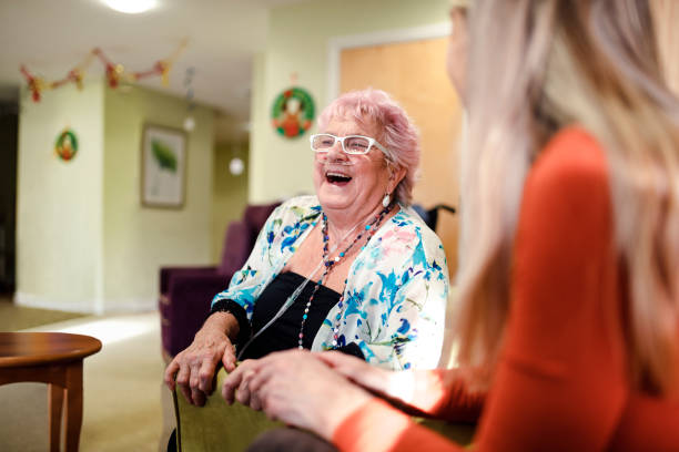 Senior woman talking to a younger woman who is visiting her while she is living in the care home. The senior woman has pink hair