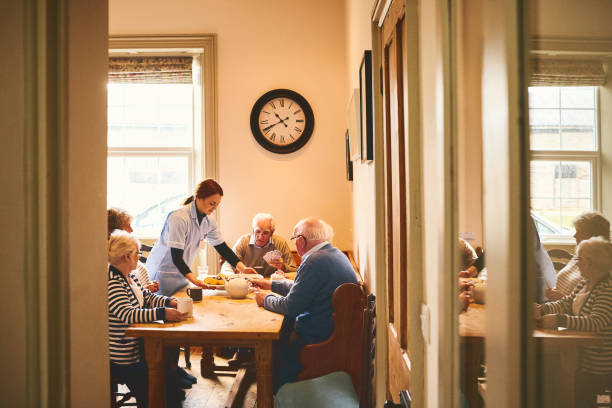 Female nurse serving food to group of senior people playing cards at nursing home
