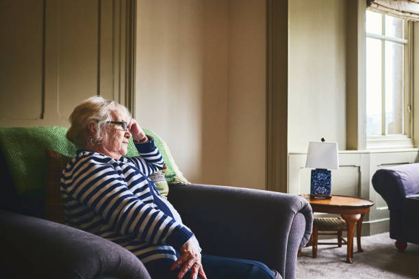 Thoughtful senior woman sitting alone on couch at home